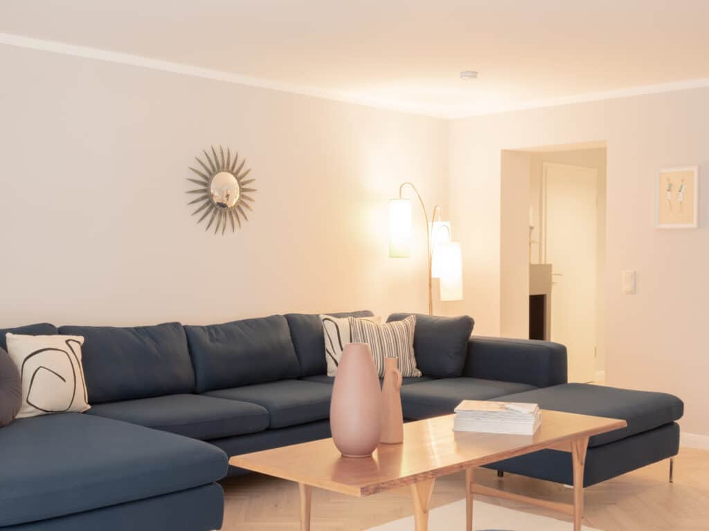 Teilansicht eines dunkelblauen Ecksofas mit gemusterten Kissen und einer brennenden Stehlampe im Hintergrund.