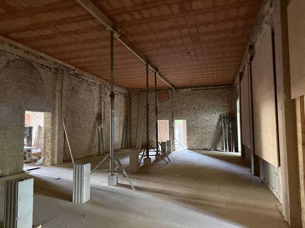 Großer Rohbau-Saal mit Ziegelsteindecke, gestützt von Stahlbaustützen, unverputzten Backsteinwänden und Rundbogenöffnungen.