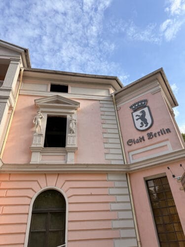 Rosa Gebäudefassade mit historischem Berliner Wappen, geschwungenem Schriftzug Stadt Berlin, Stuckfiguren und Sprossenfenster.