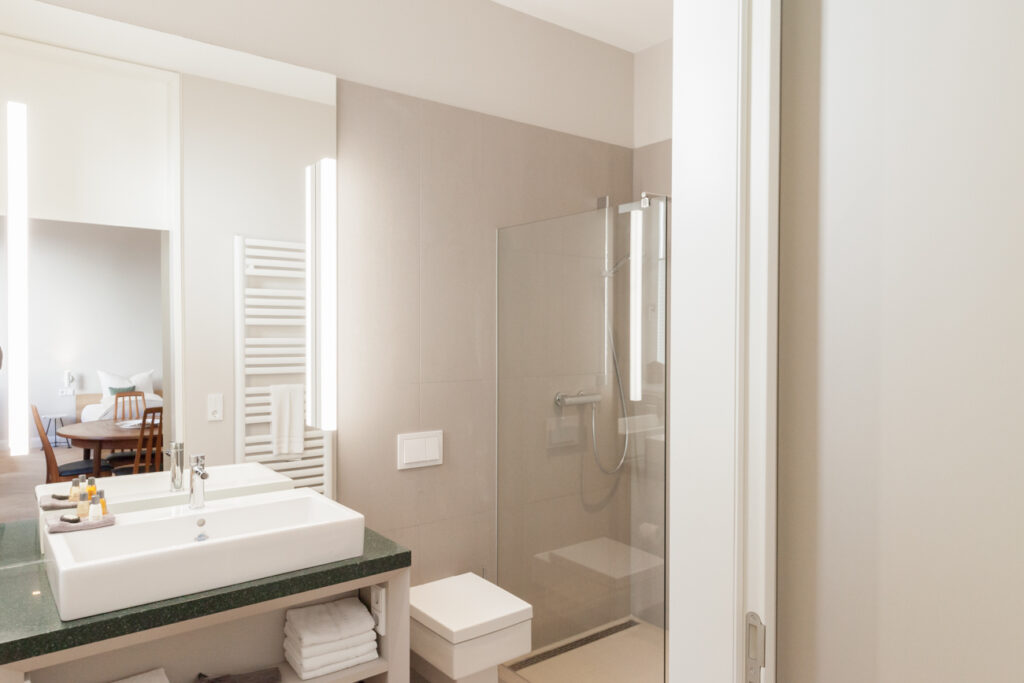 Detailansicht eines modernen Badezimmers mit einer verglasten, begehbaren Dusche und weißem Handtuchtrockner in der Usedom Villa Staudt.