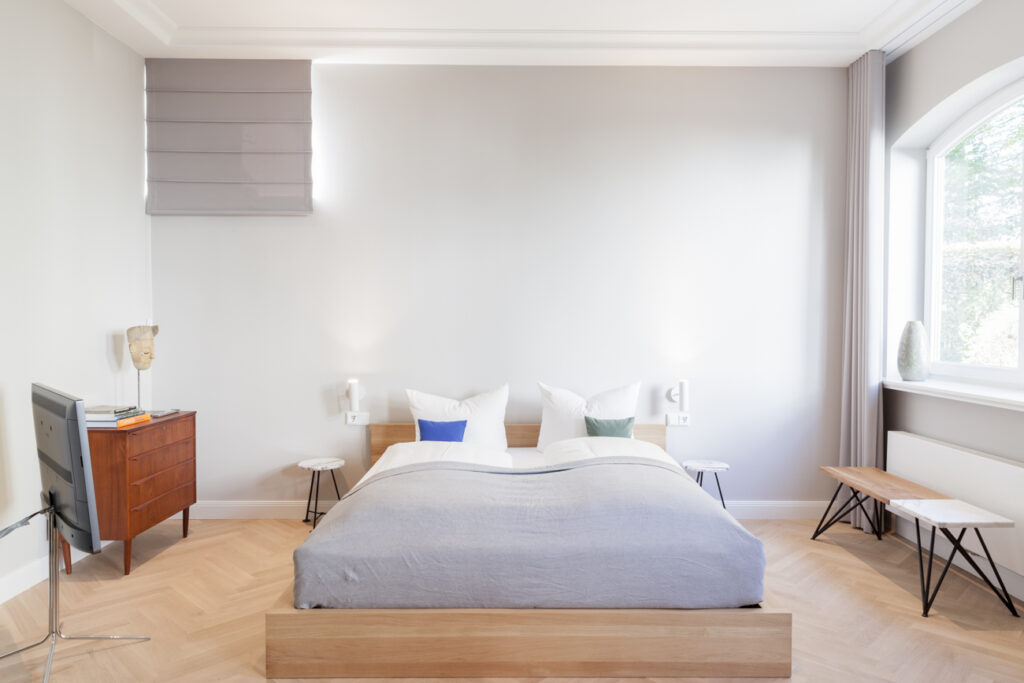Ein aufgeräumtes Schlafzimmer mit einem breiten Bett, Holzboden und einem minimalistischen Kommoden im Usedom Loft der Villa Staudt.