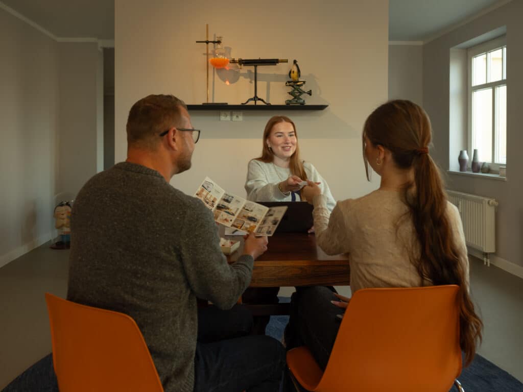 Eine Mitarbeiterin reicht einem Gast eine Zimmerkarte über einen Holztisch mit Informationsbroschüren.