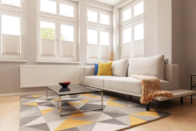 Heller Wohnbereich im Apartment 6 mit großem beigem Sofa, Glas-Couchtisch und modernem Teppich vor einer hohen Fensterfront.