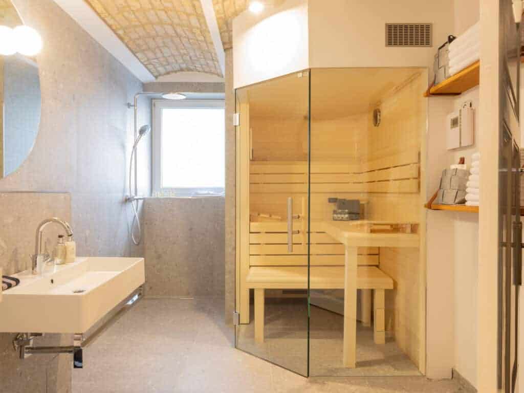 Helles Badezimmer mit historischem Backsteingewölbe, modernem Waschtisch, Regendusche und einer verglasten Holzsauna.