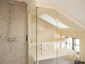 Modern gefliestes Badezimmer mit Regendusche aus Chrom und angrenzender, vollverglaster Sauna unter einem Dachflächenfenster.